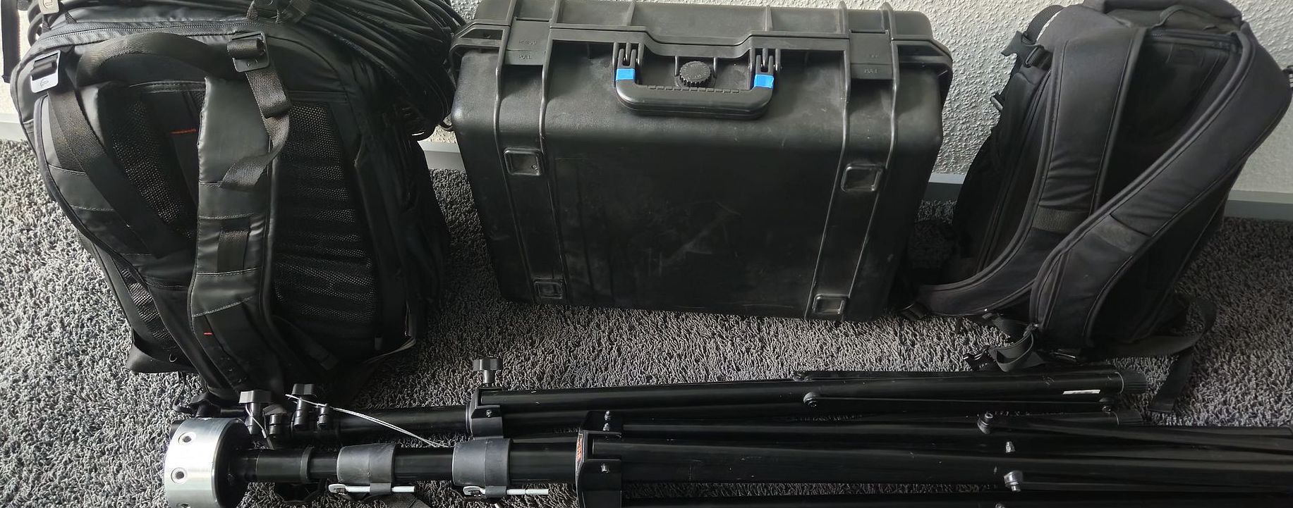 A big backpack, a hand case, a small backpack and two light stands in the front
